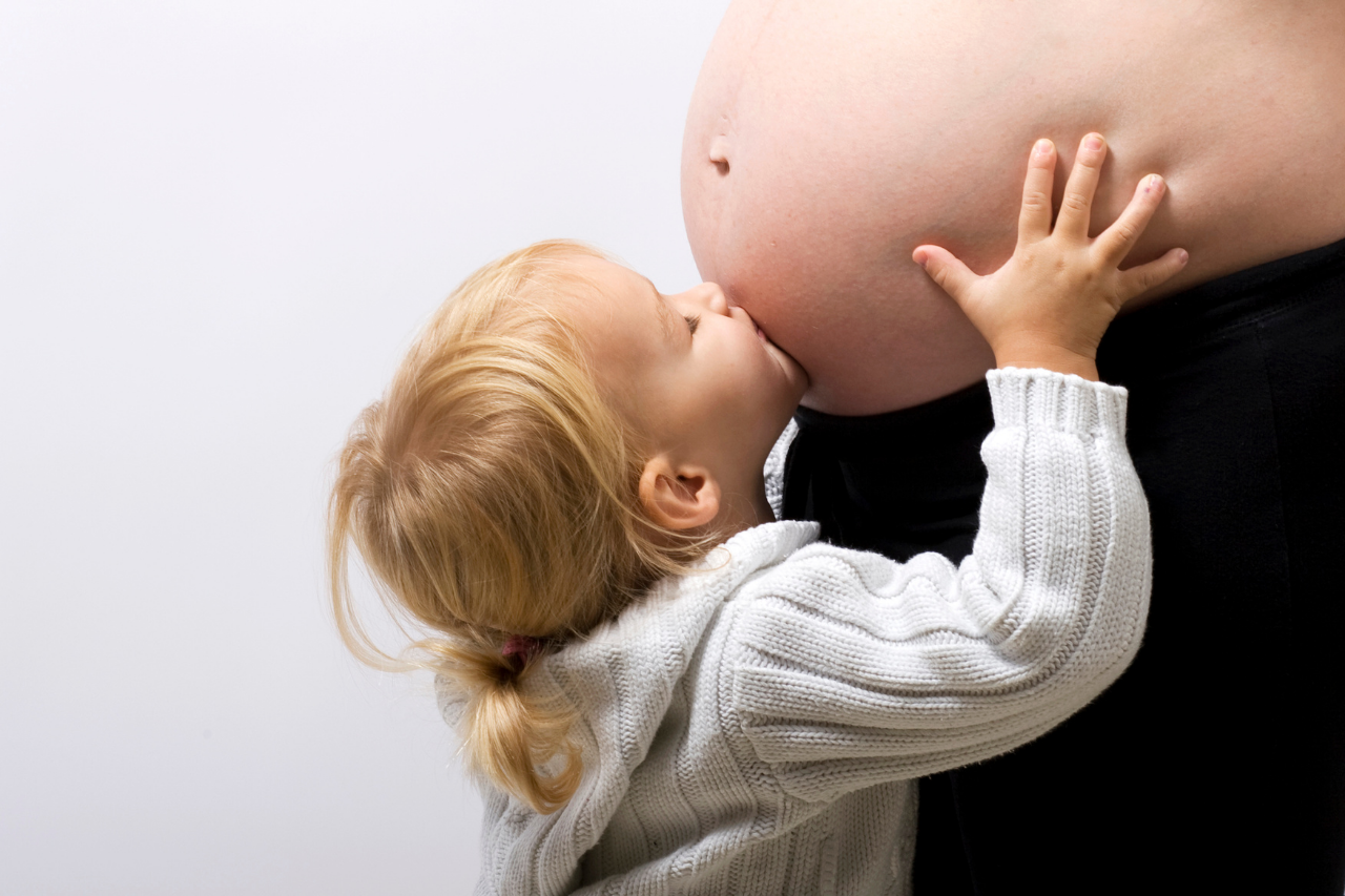 A young child embracing a pregnant mothers tummy