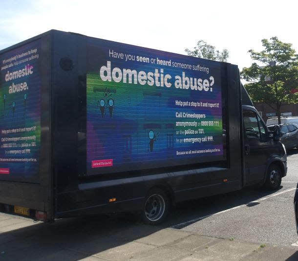 An image of Salford's domestic abuse advertisement van, which is displaying messages about domestic abuse and the support available to help victims. The van creative is coloured in green, blue and purple.
