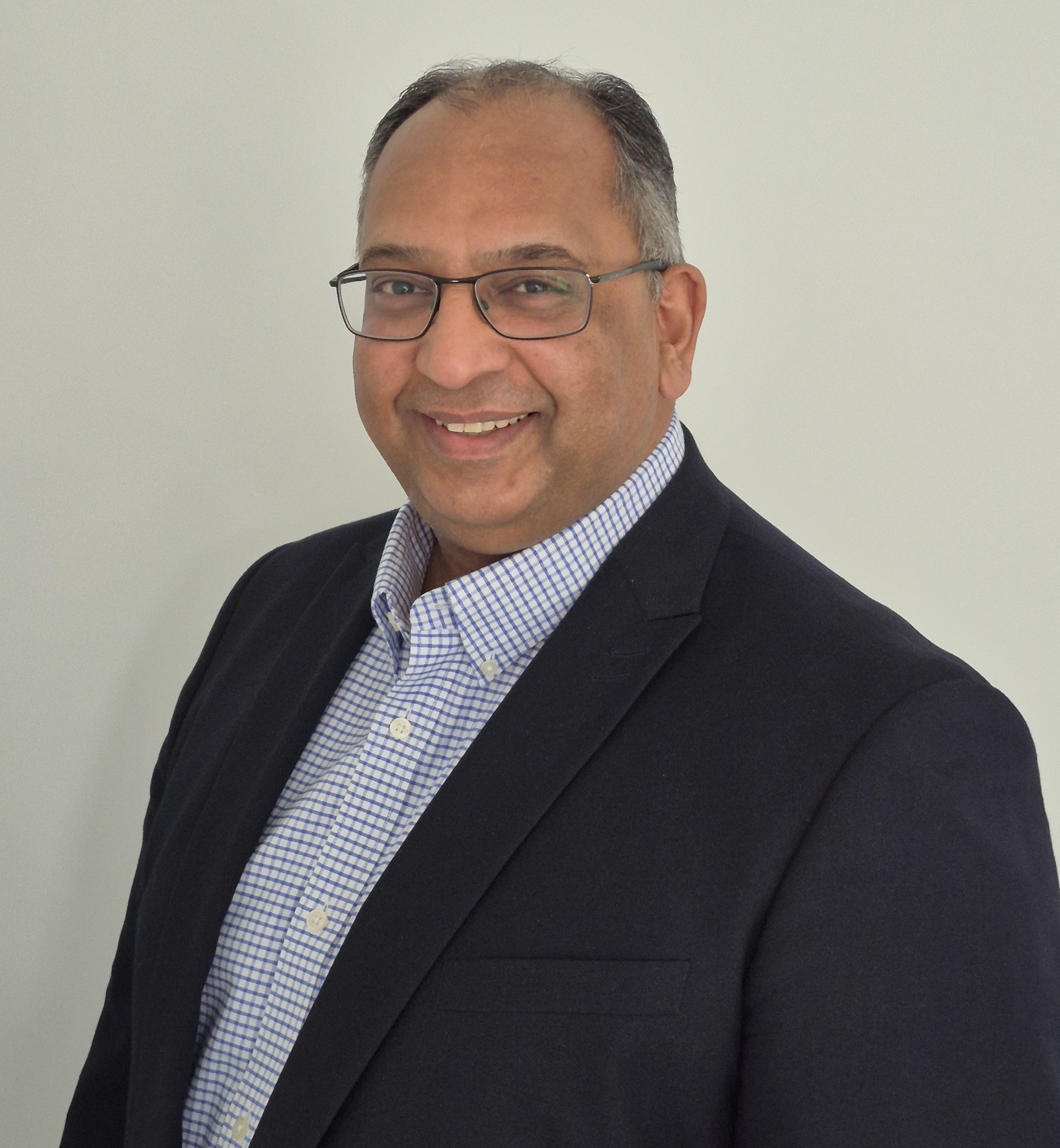 Surjit Tour, wearing blue jacket and checked shirt, smiling