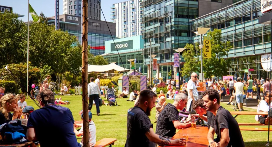 People at park benches in the sun at The Quays and MediaCity in Salford
