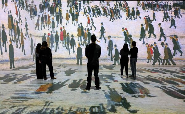 Silhouettes of people stood in an immersive gallery experience showing Lowry stick figures on every surface