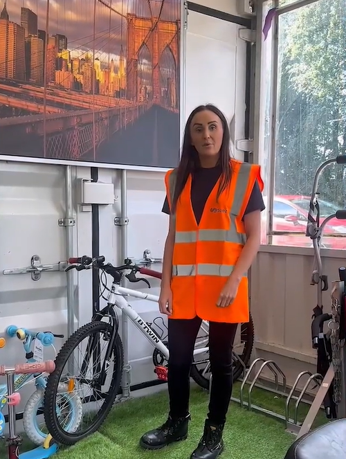 A woman wearing a high vis vest stands in front of goods for sale