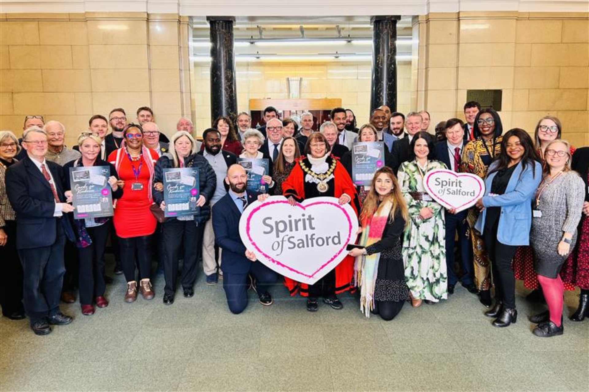City Mayor Paul Dennett, Deputy Mayor Tracey Kelly, Councillor Heather Fletcher, Ceremonial Mayor of Salford, Councillor Mishal Saeed and along with Councillors and officers from across the City Council. Holding the Spirit of Salford emblem and posters to promote the Cards for Kindness campaign.
