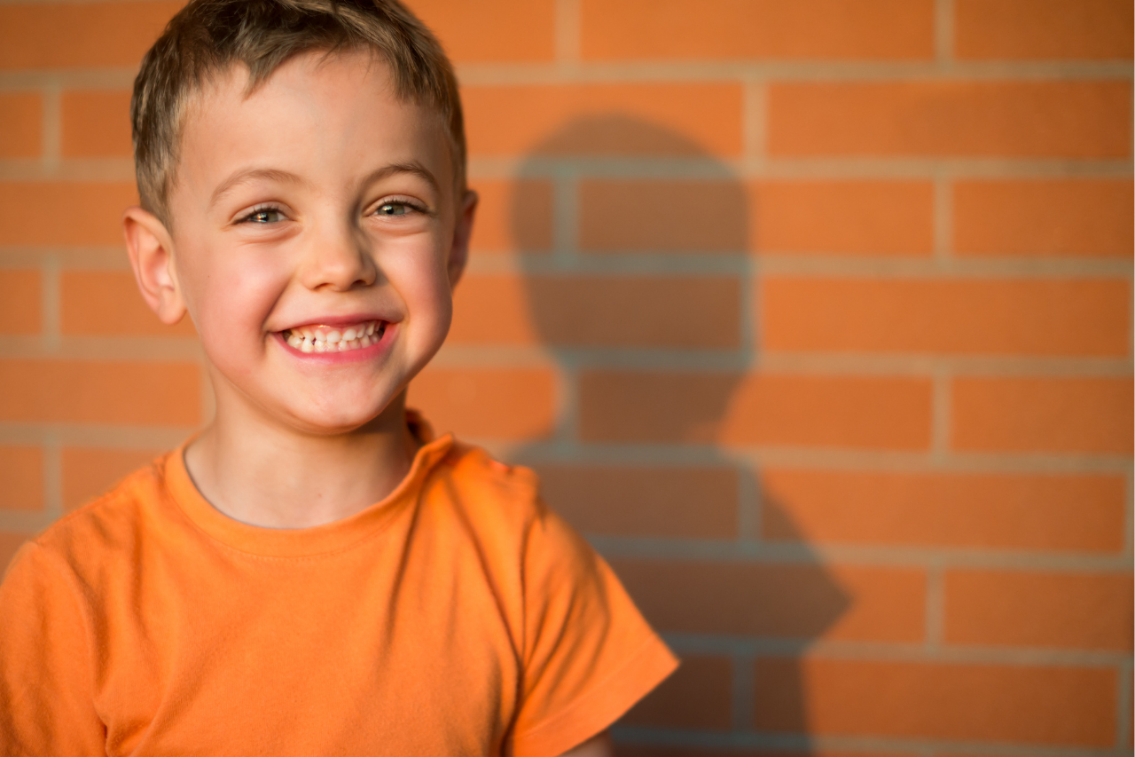 a young boy wearing a bright orange t-shirt and smiling