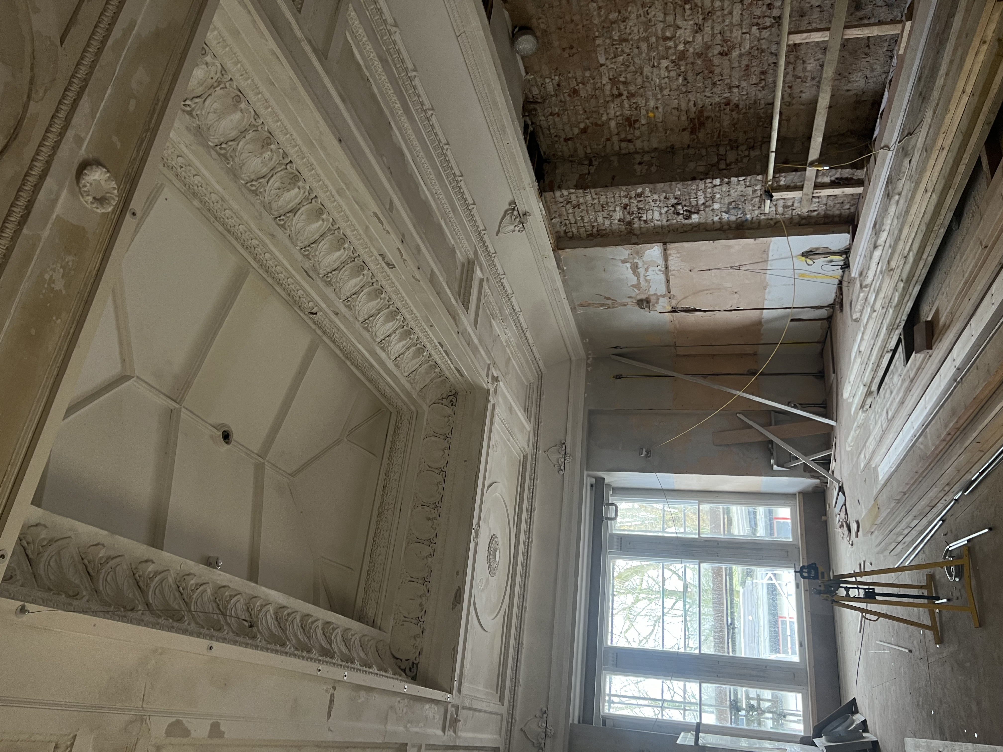 Image of Buile Hill mansion restorations with ornate ceilings and coving being lovingly and carefully restored. Also in the image are exposed brick walls and building materials.