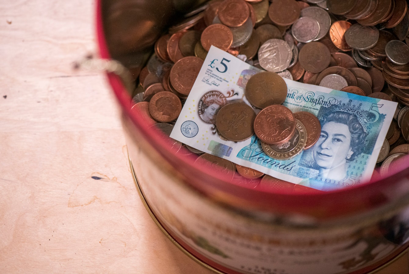 A tin holding a £5 note and many assorted coins