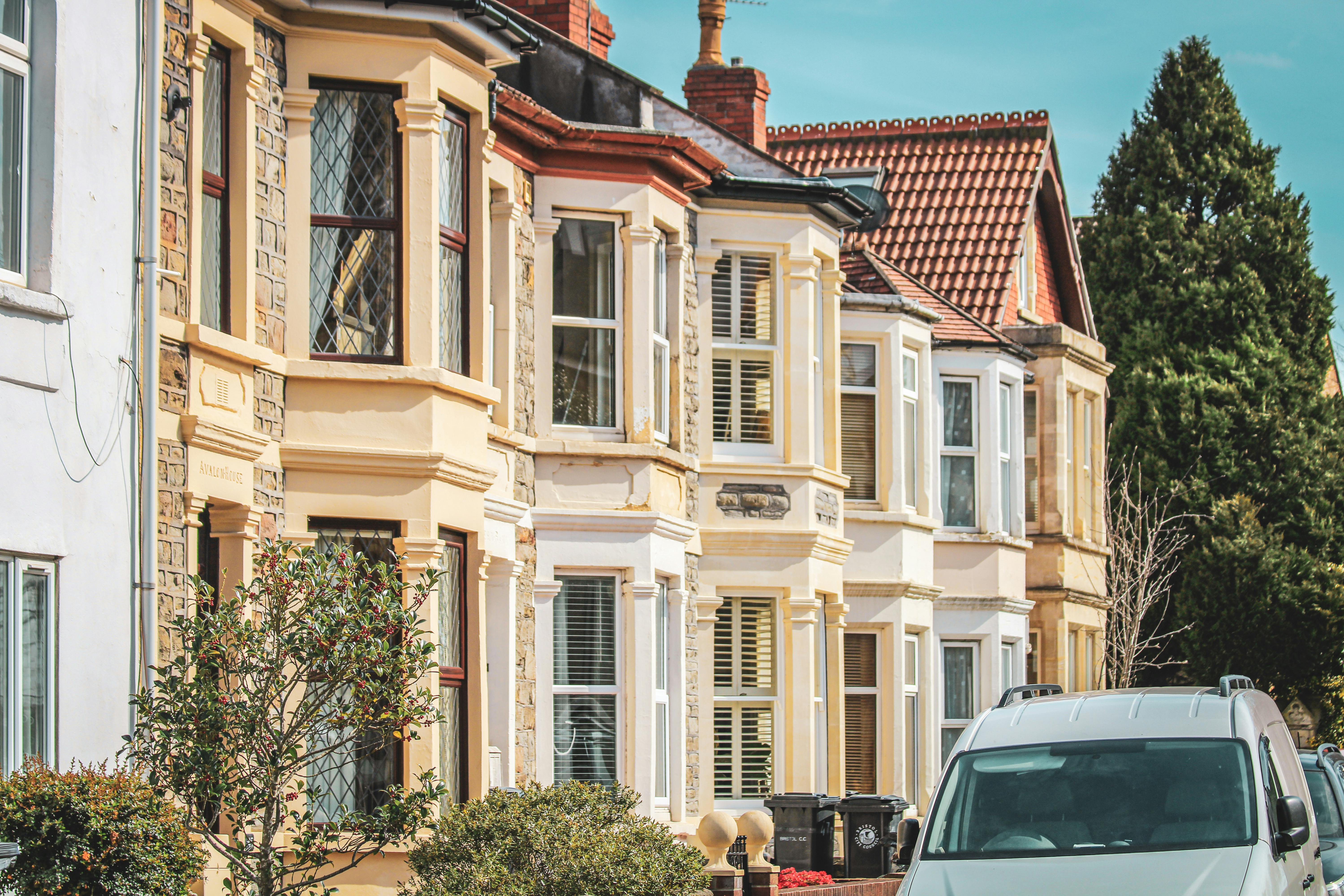 Row of houses with van and cars parked outside on street close to tall trees