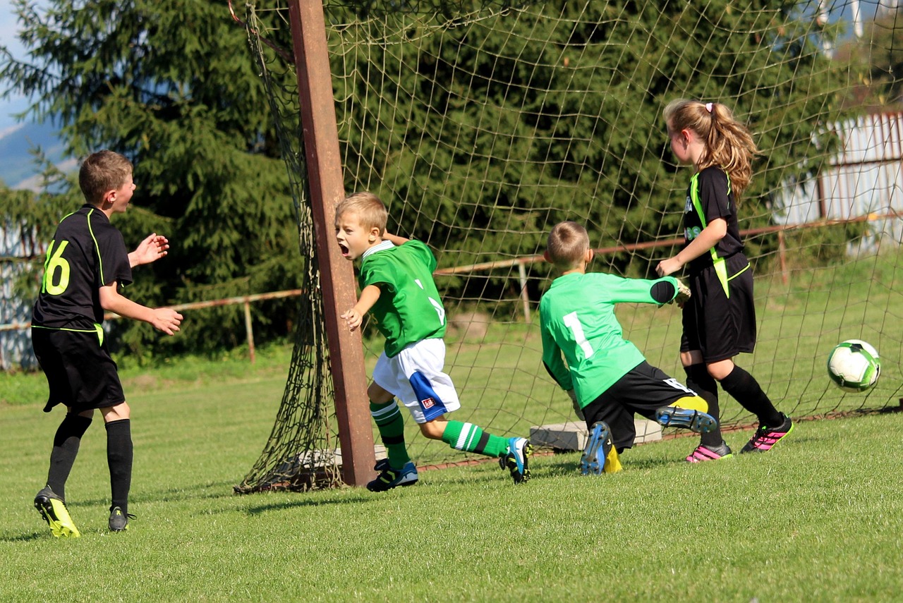 girls and boys playing football in a green space near the net