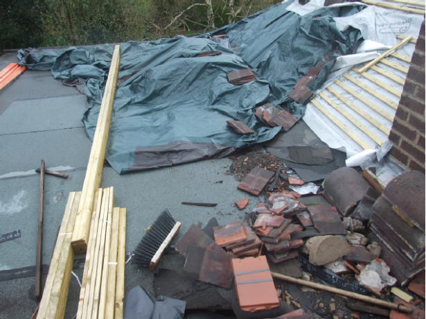 Roof with tarpaulin covering and pile of roof tiles